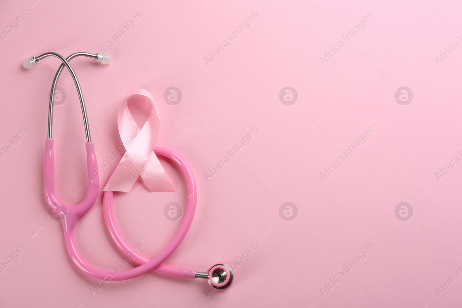 Photo of Pink ribbon as breast cancer awareness symbol and stethoscope on color background, flat lay. Space for text