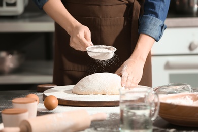 Photo of Woman sprinkling flour over dough on table in kitchen