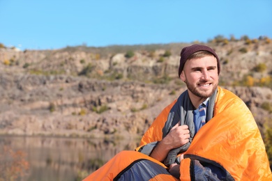 Young male camper in sleeping bag outdoors. Space for text