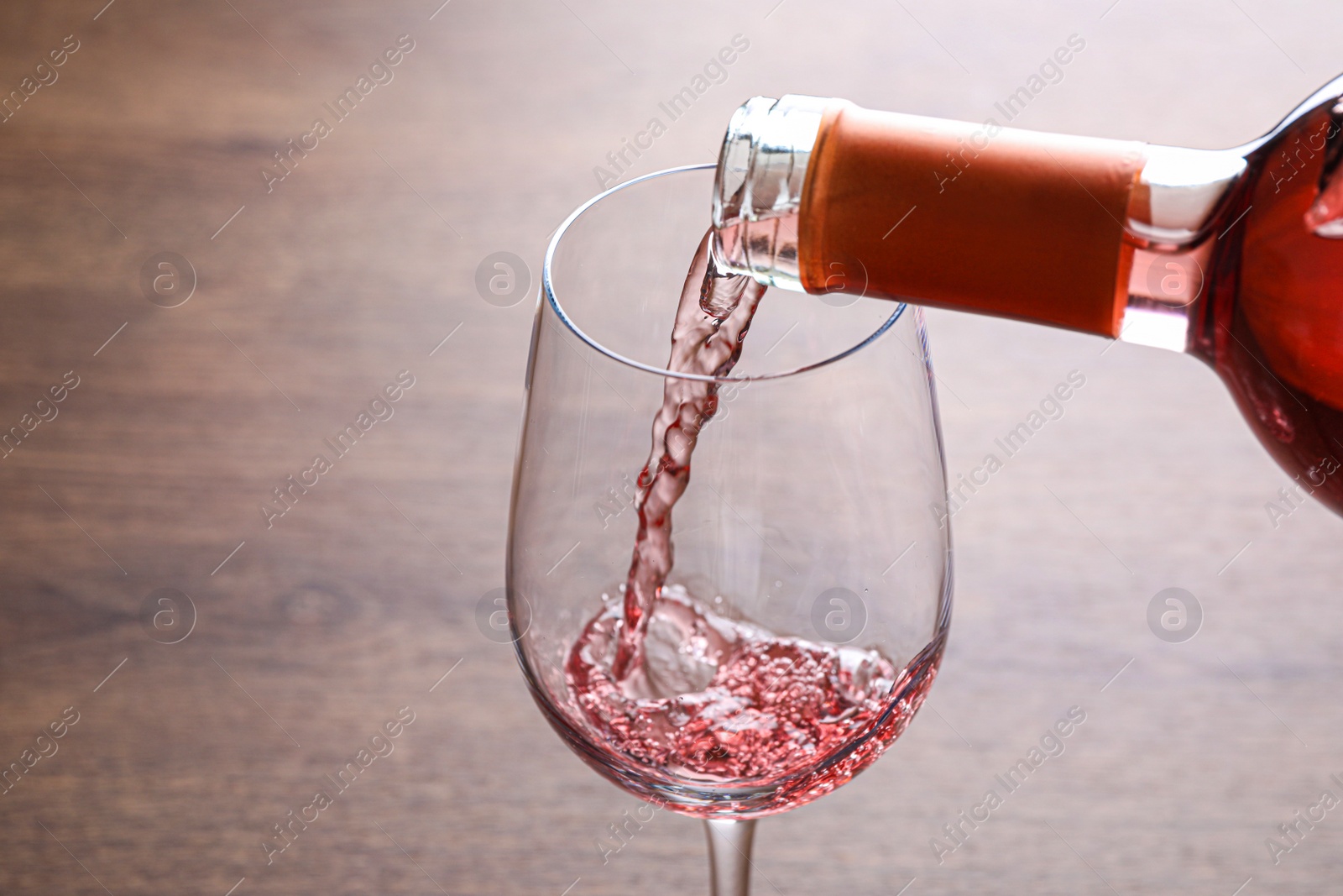 Photo of Pouring delicious rose wine into glass on wooden table, closeup