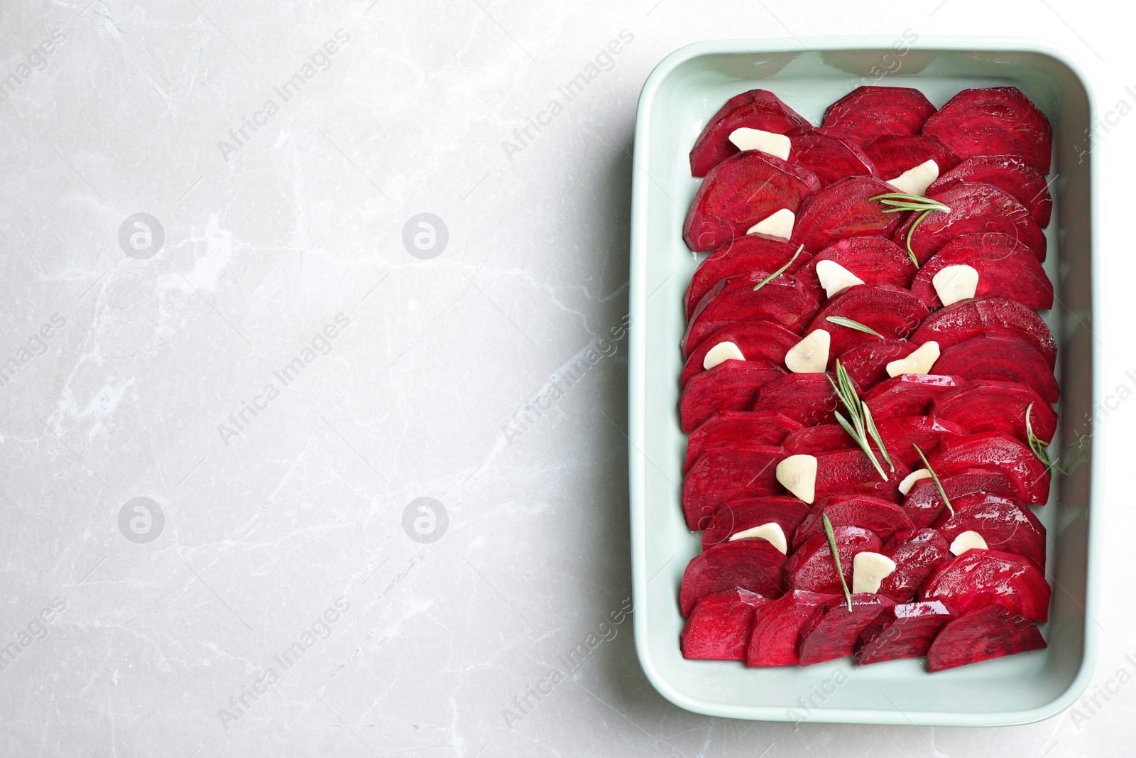 Photo of Baking dish with raw beetroot slices, garlic and rosemary on light marble table, top view. Space for text