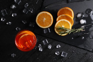 Glass of tasty Aperol spritz cocktail with orange slices and ice cubes on black table, flat lay