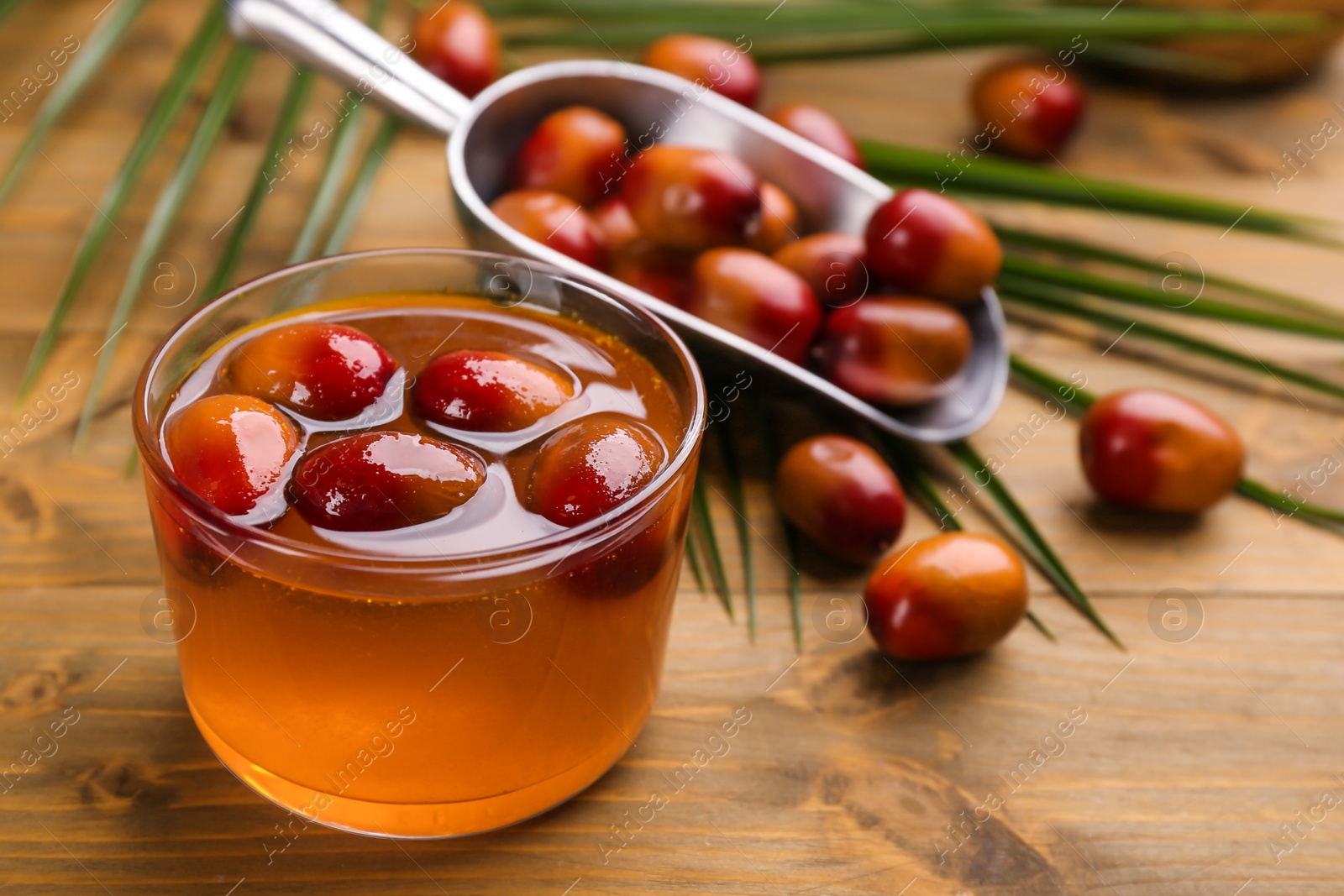 Photo of Palm oil in glass bowl with fruits and tropical leaf on wooden table. Space for text