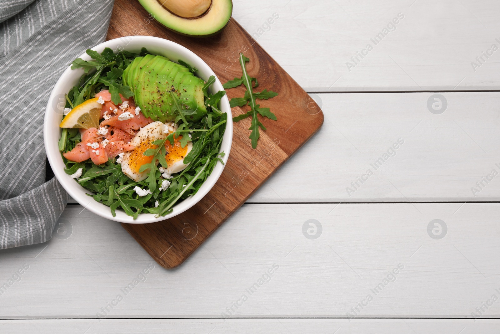 Photo of Delicious salad with boiled egg, salmon and avocado served on white wooden table, flat lay. Space for text