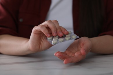 Woman taking antidepressant pill out from blister at white marble table, closeup