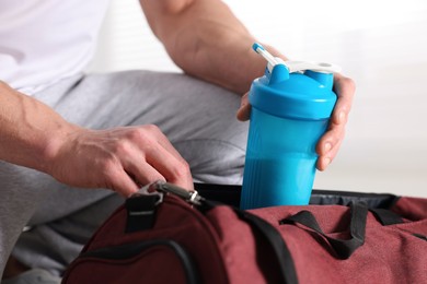 Photo of Young man putting shaker with protein into bag on blurred background, closeup