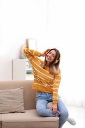 Photo of Young woman in headphones enjoying music on sofa at home