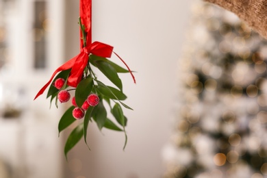 Photo of Mistletoe bunch with red bow hanging indoors, space for text. Traditional Christmas decor