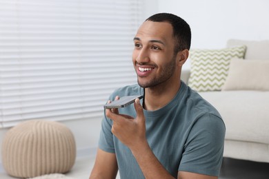 Photo of Happy man sending voice message via smartphone indoors