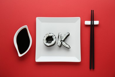 Photo of Word Ok made of sushi rolls, chopsticks and soy sauce on red background, flat lay