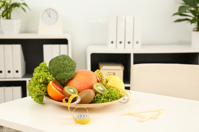 Photo of Nutritionist's workplace with fruits, vegetables, measuring tape and body fat caliper on table