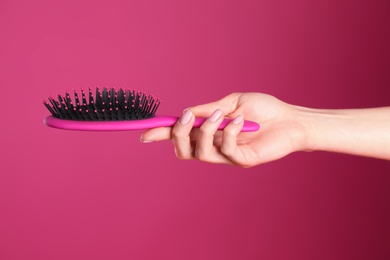 Photo of Woman holding hair brush against crimson background, closeup