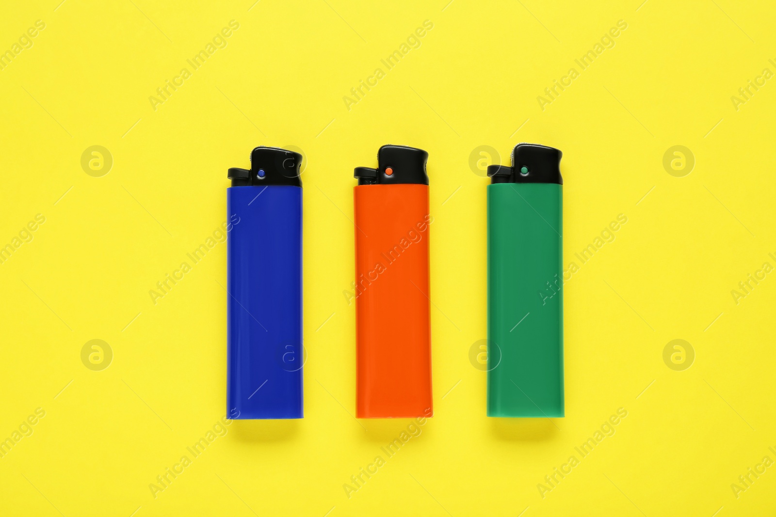 Photo of Stylish small pocket lighters on yellow background, flat lay