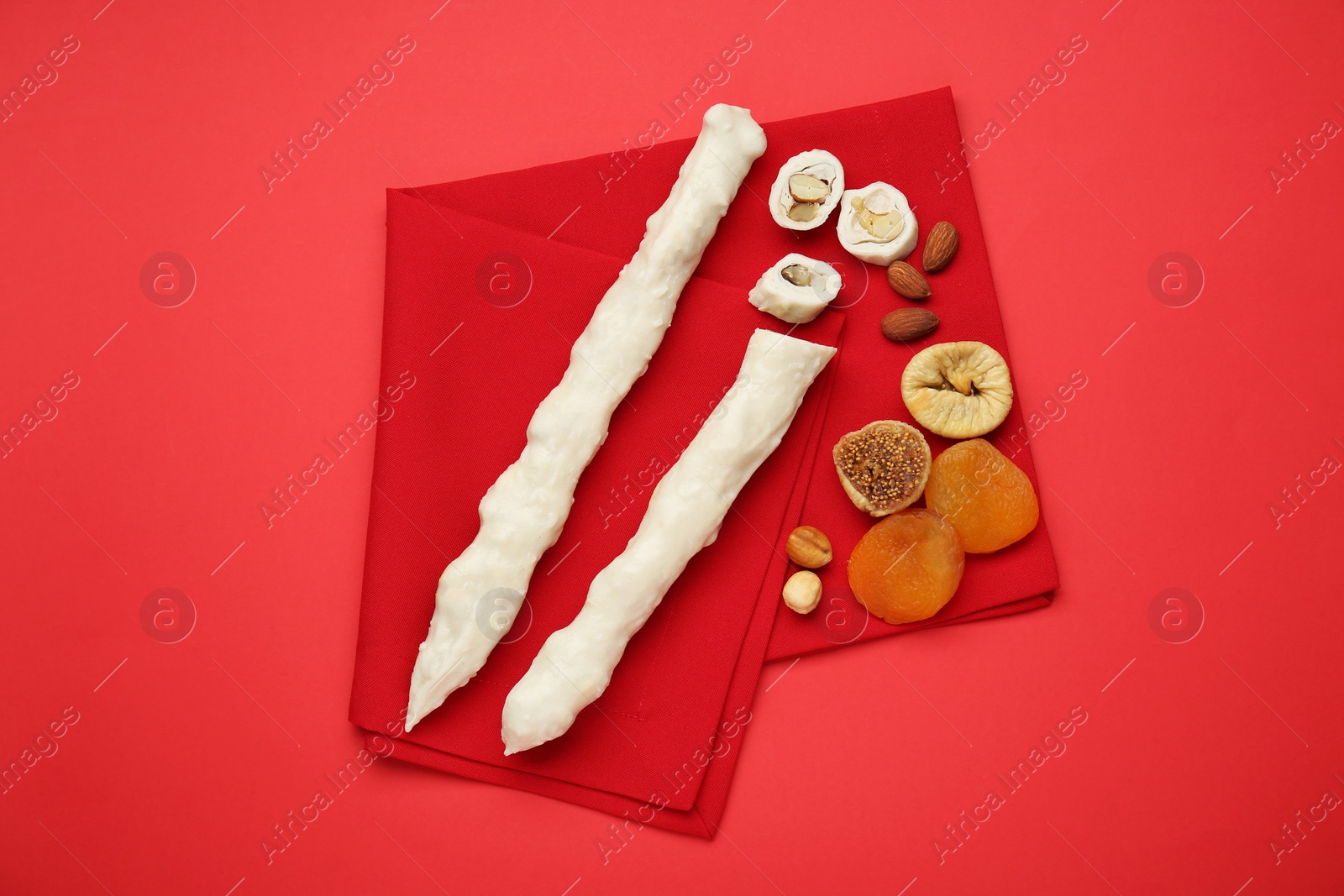 Photo of Delicious churchkhelas, nuts and dried fruits on red background, top view