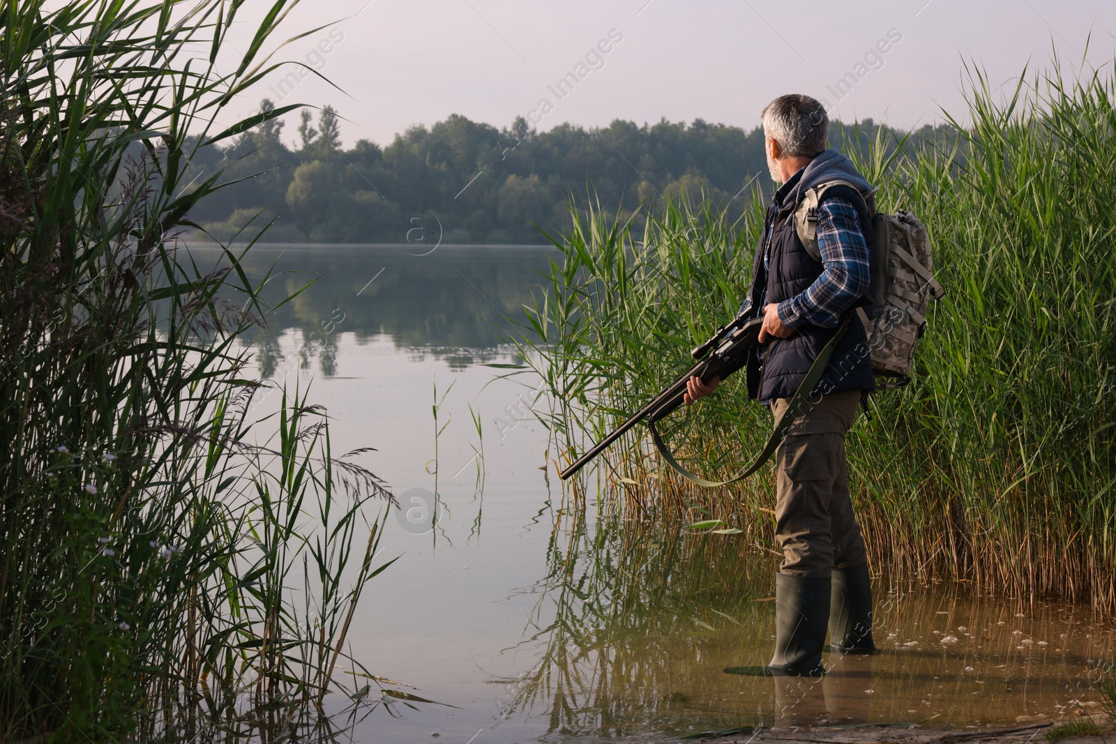 Photo of Man with hunting rifle near lake outdoors. Space for text