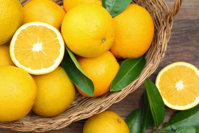 Wicker basket, ripe juicy oranges and green leaves on wooden table, flat lay