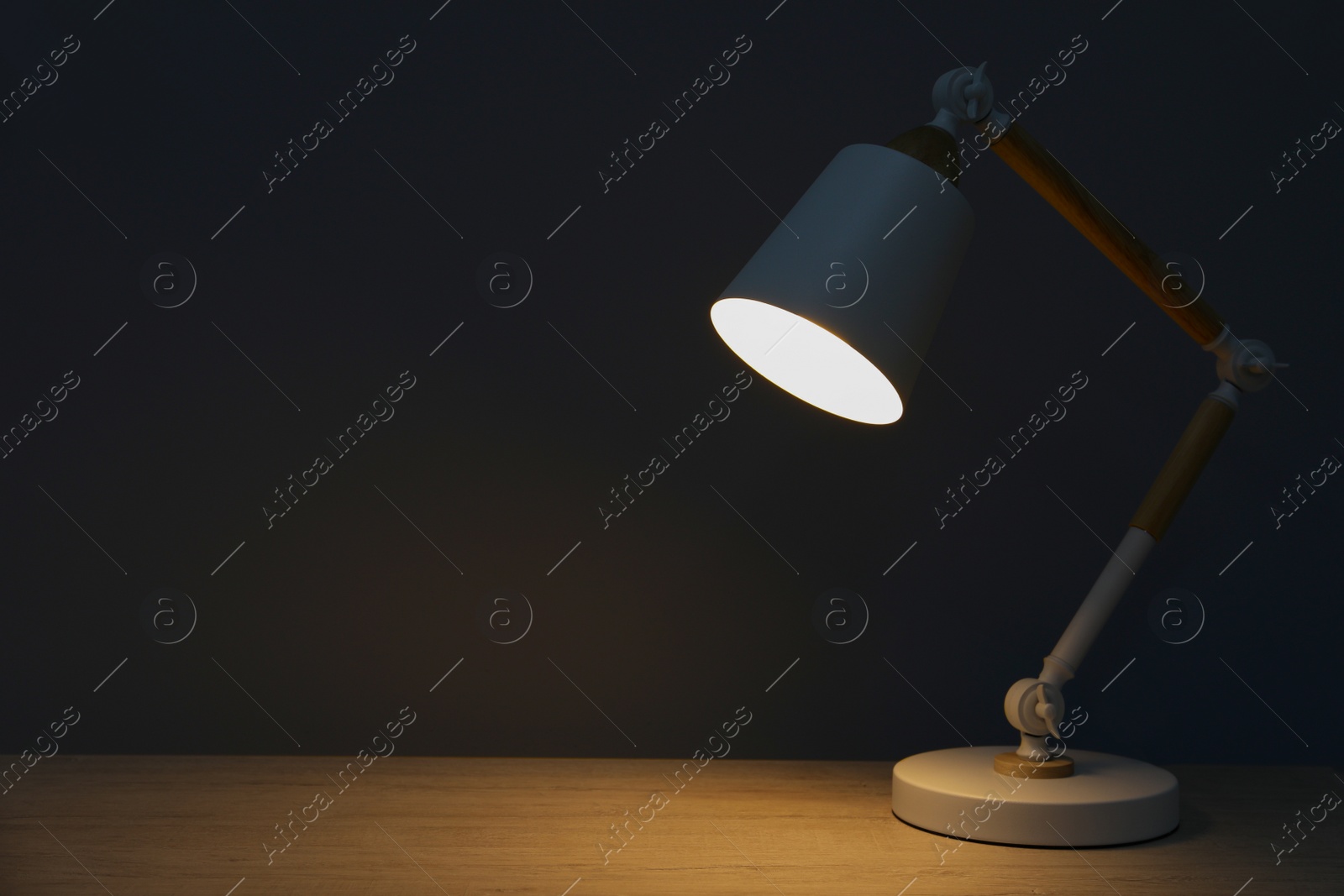 Photo of Stylish modern desk lamp on wooden table at night, space for text