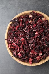 Photo of Hibiscus tea. Wooden bowl with dried roselle calyces on grey table, top view