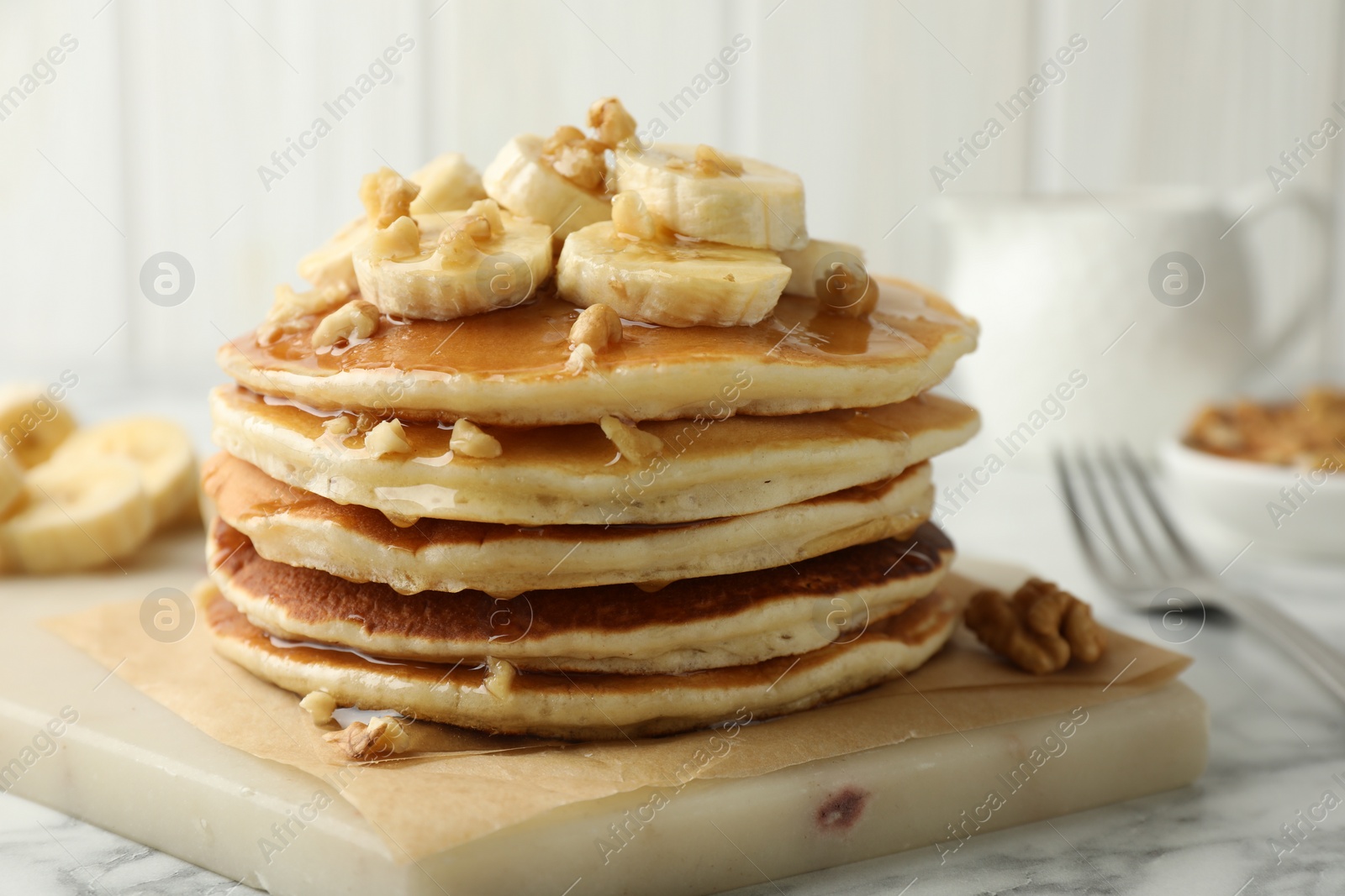 Photo of Delicious pancakes with bananas, walnuts and honey on white marble table, closeup