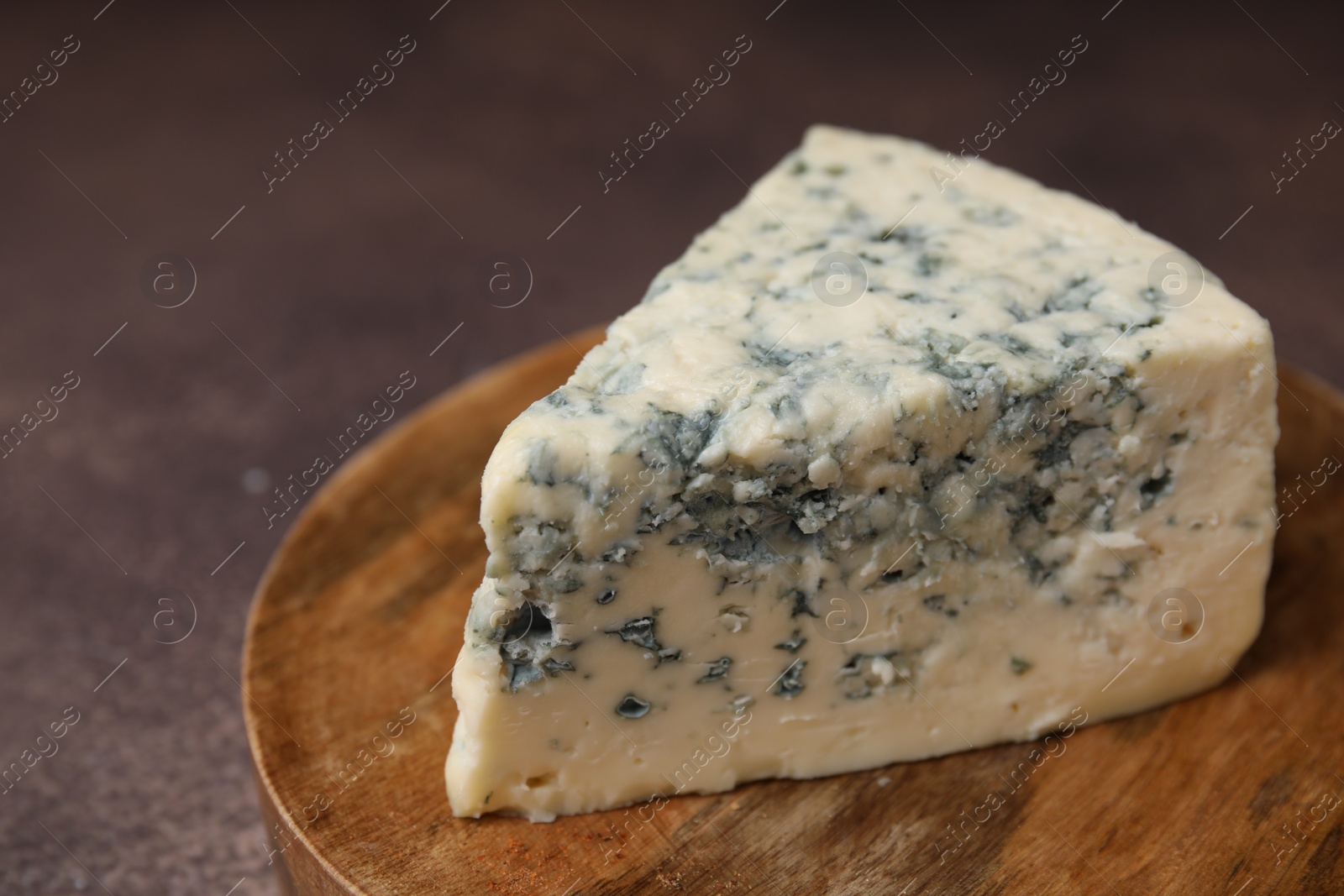 Photo of Piece of tasty blue cheese on brown table, closeup. Space for text