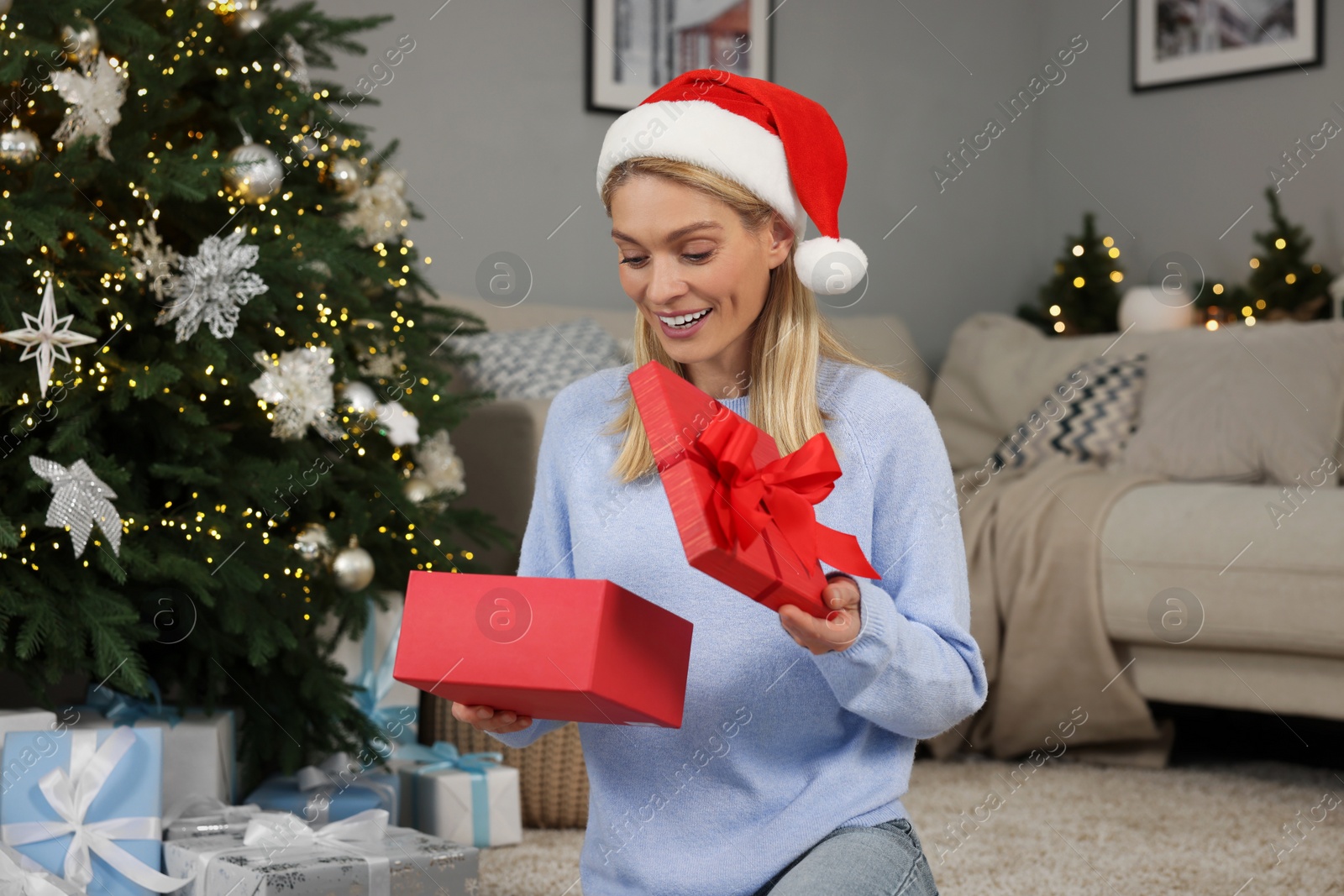 Photo of Happy woman in Santa hat opening Christmas gift at home