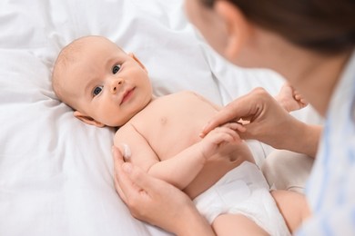 Woman applying body cream onto baby`s skin on bed, above view