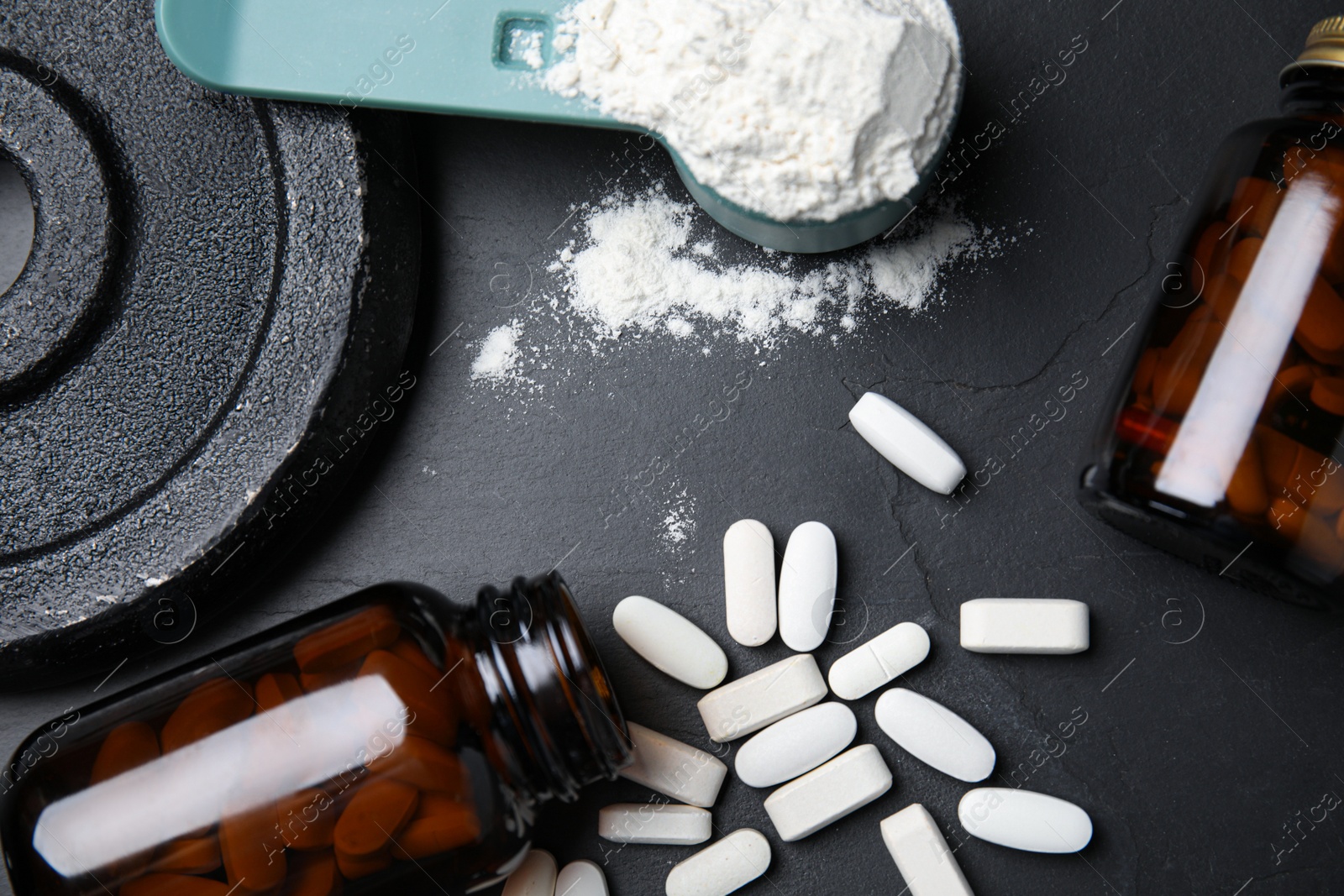 Photo of Pills, measuring scoop of amino acids powder and weight plates on black table, flat lay