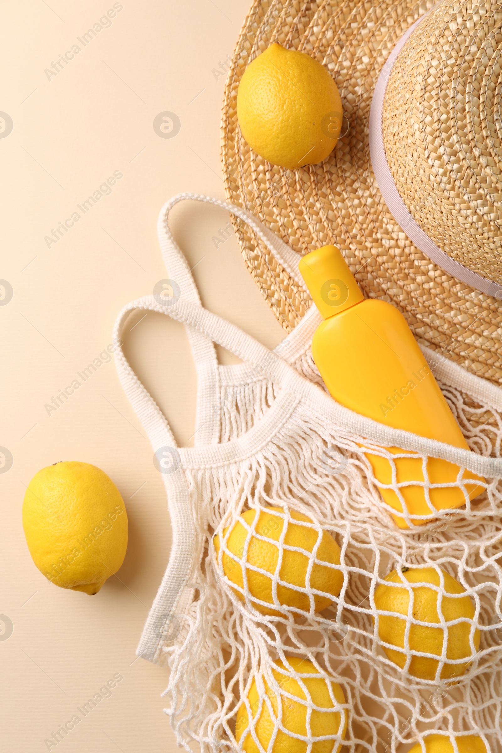 Photo of String bag with fresh lemons, sunscreen and straw hat on beige background, flat lay