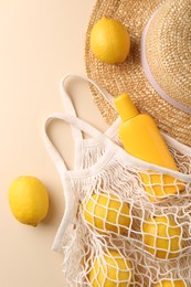 String bag with fresh lemons, sunscreen and straw hat on beige background, flat lay