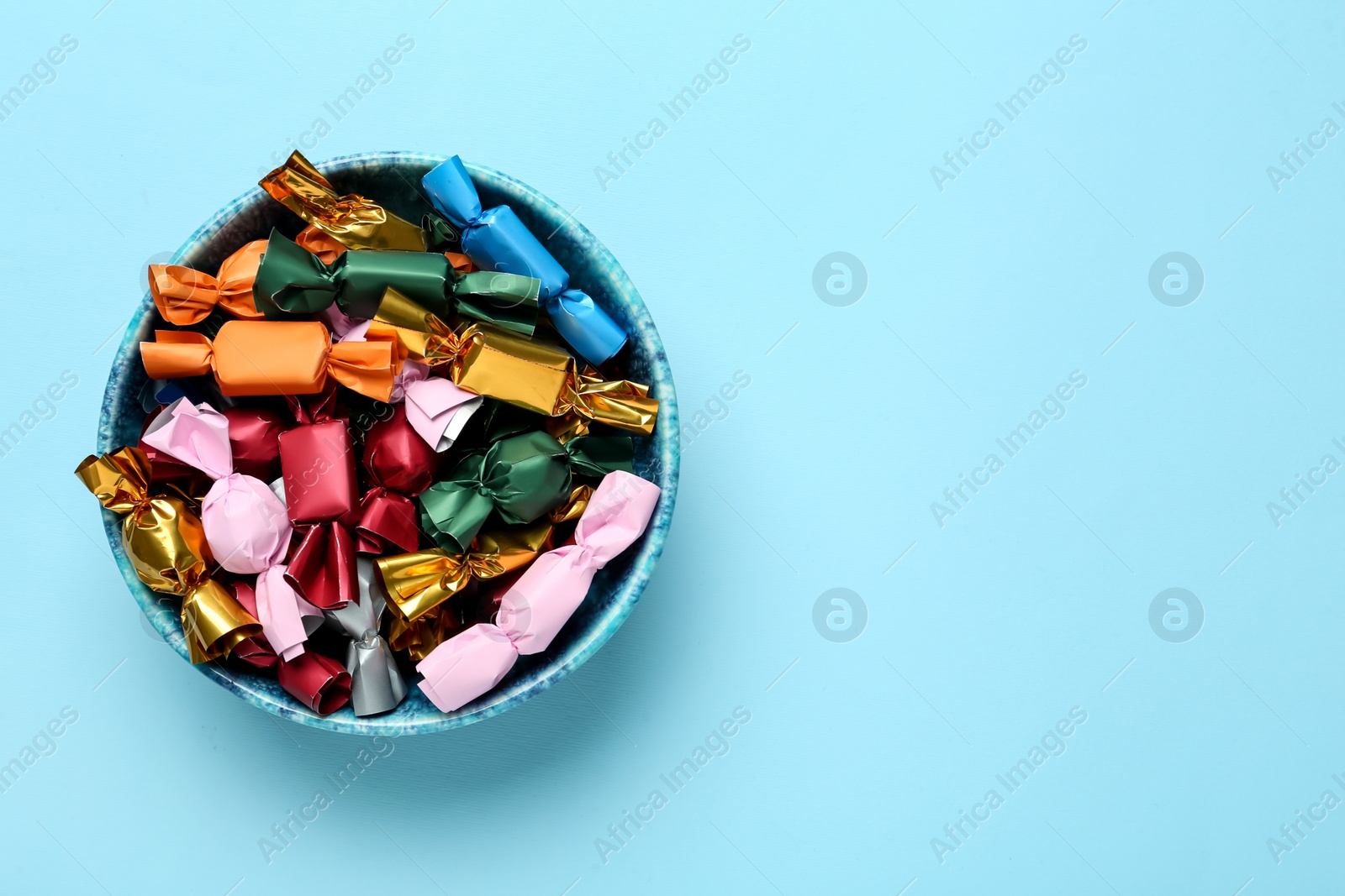 Photo of Candies in colorful wrappers on light blue background, top view. Space for text