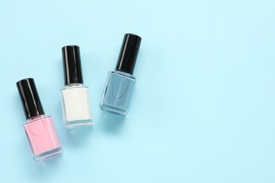 Bright nail polishes in bottles on light blue background, flat lay. Space for text