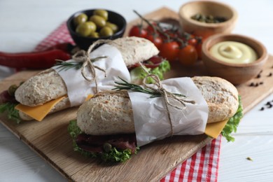 Photo of Delicious sandwiches with bresaola, cheese and other products on white wooden table
