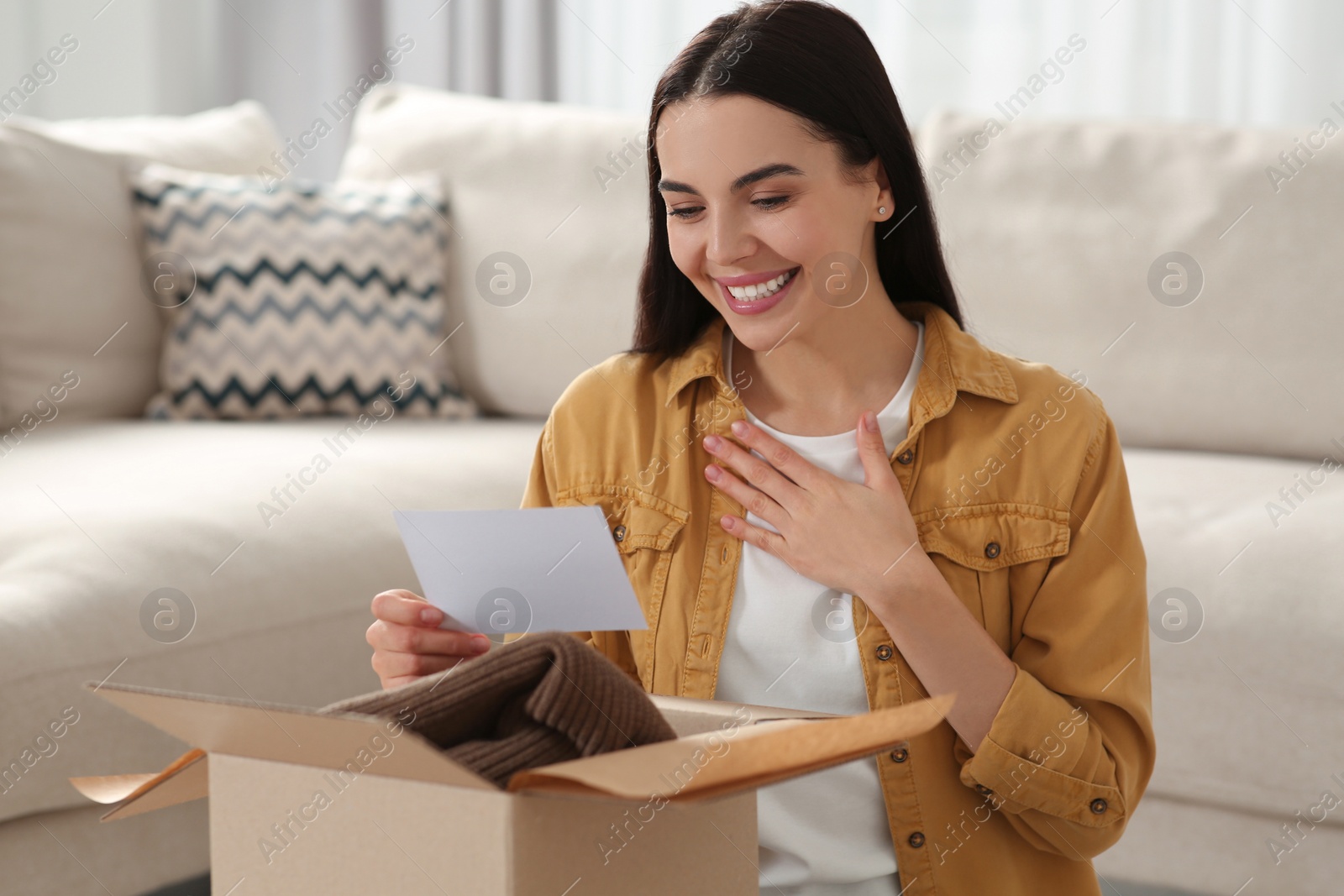 Photo of Happy woman holding greeting card near parcel with Christmas gift at home