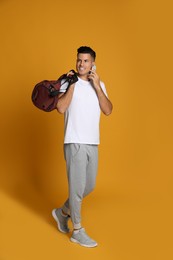 Photo of Handsome man with sports bag and smartphone on yellow background