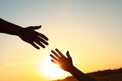 Man giving hand to woman outdoors at sunset, closeup. Help and support concept