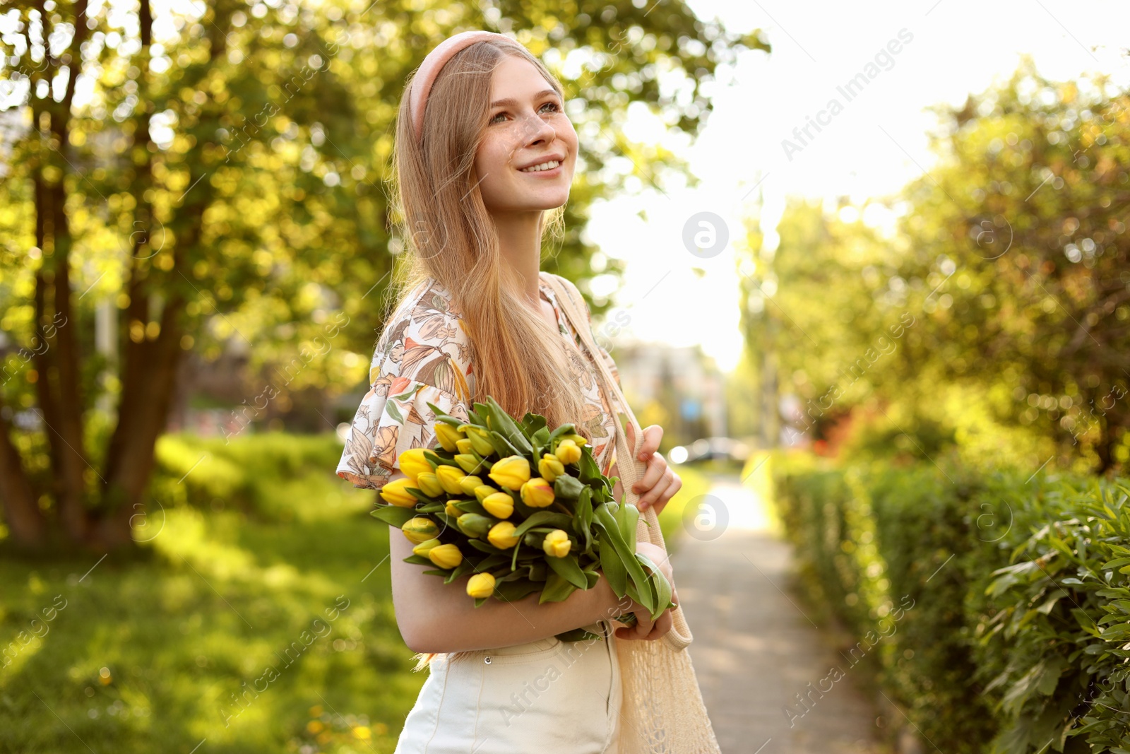 Photo of Beautiful teenage girl with bouquet of yellow tulips in park on sunny day