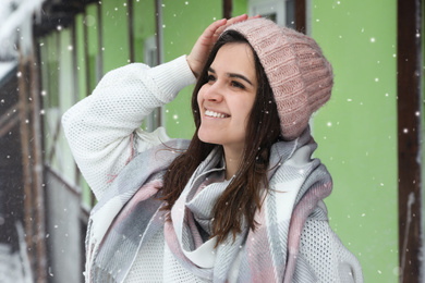 Photo of Young woman wearing warm sweater and scarf  outdoors on snowy day. Winter season