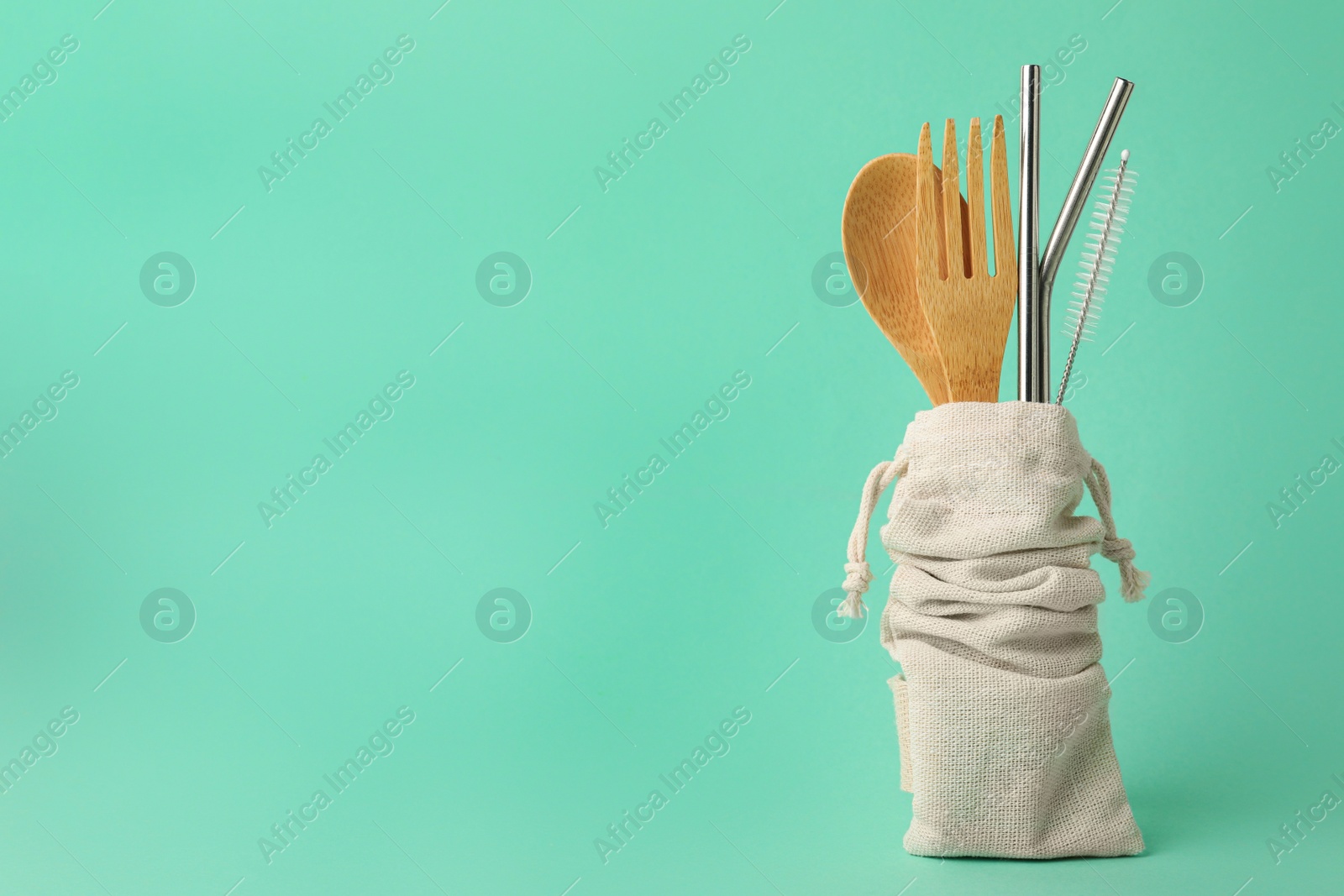 Photo of Bag with bamboo cutlery, metal straws and brush on turquoise background, space for text. Conscious consumption