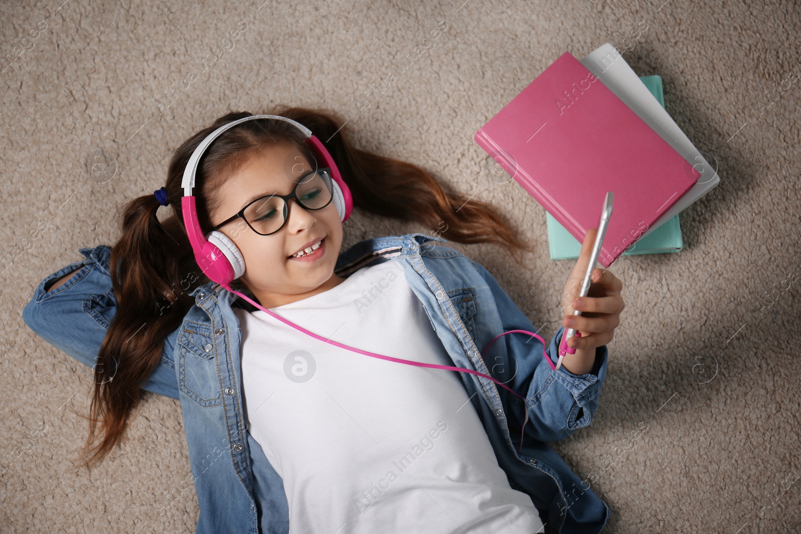 Photo of Cute little girl listening to audiobook on floor, top view