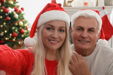 Photo of Happy mature couple in Santa hats taking selfie at home. Christmas celebration