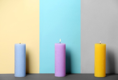 Decorative wax candles on table against color background