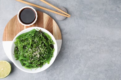 Photo of Tasty seaweed salad in bowl served on gray table, flat lay. Space for text