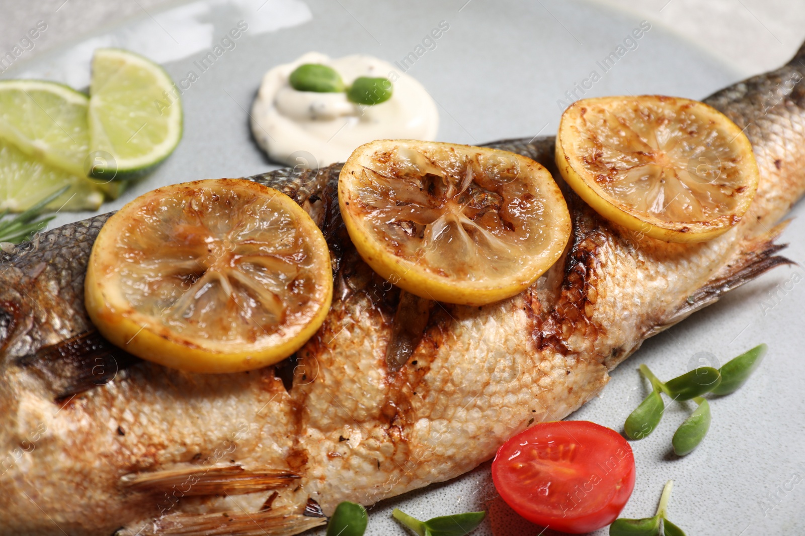 Photo of Delicious roasted sea bass fish served with lemon, tomatoes and sauce, closeup