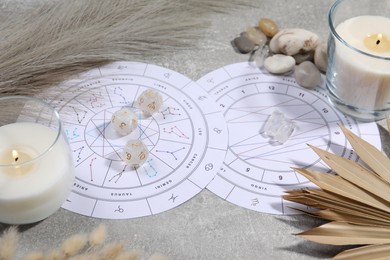 Photo of Zodiac wheel, natal chart, burning candles, astrology dices and stones on grey table