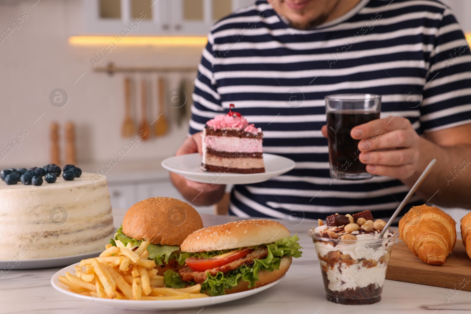 Photo of Overweight man with glass of cold drink and cake at table in kitchen, closeup