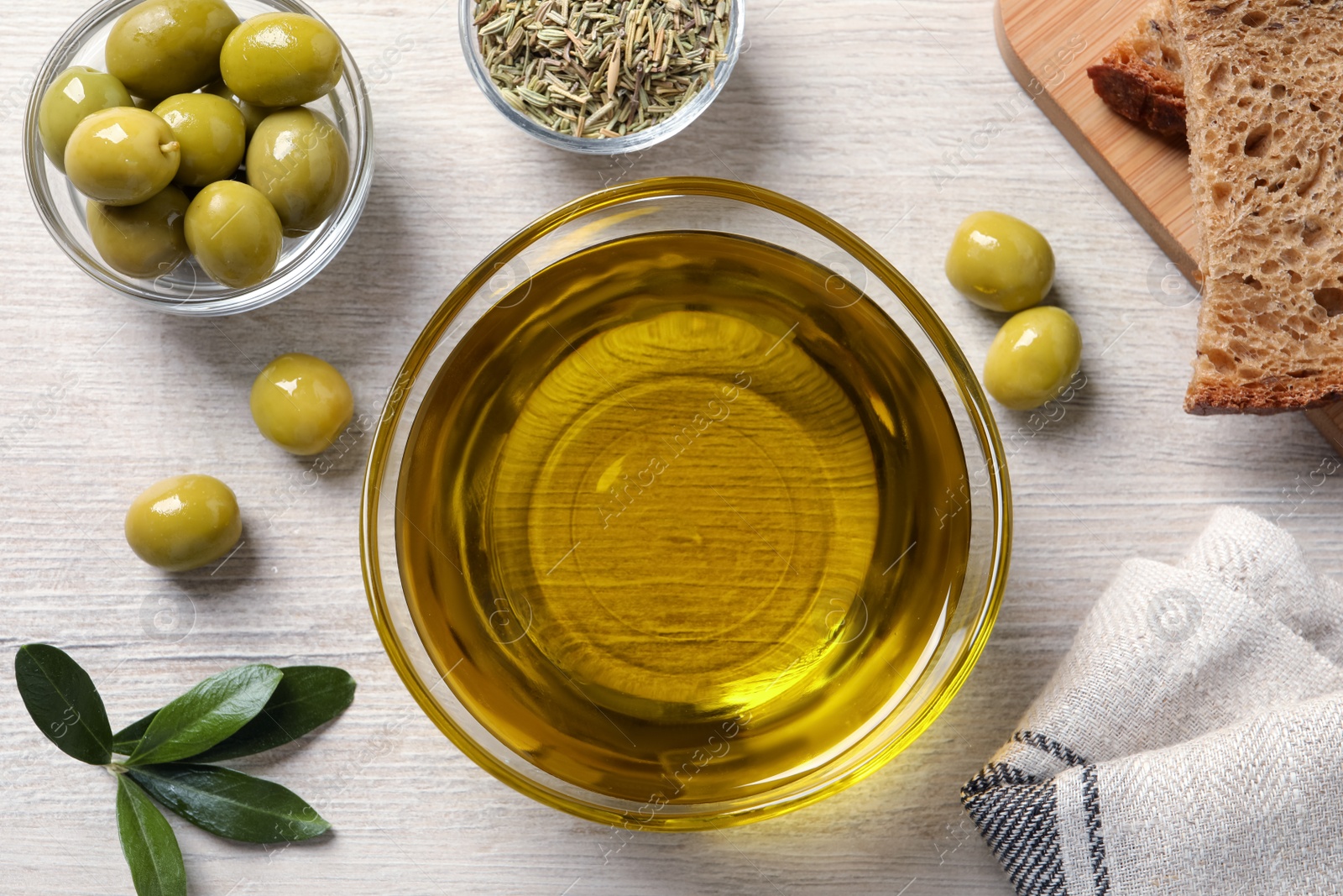 Photo of Glass bowl with fresh olive oil on white wooden table, flat lay