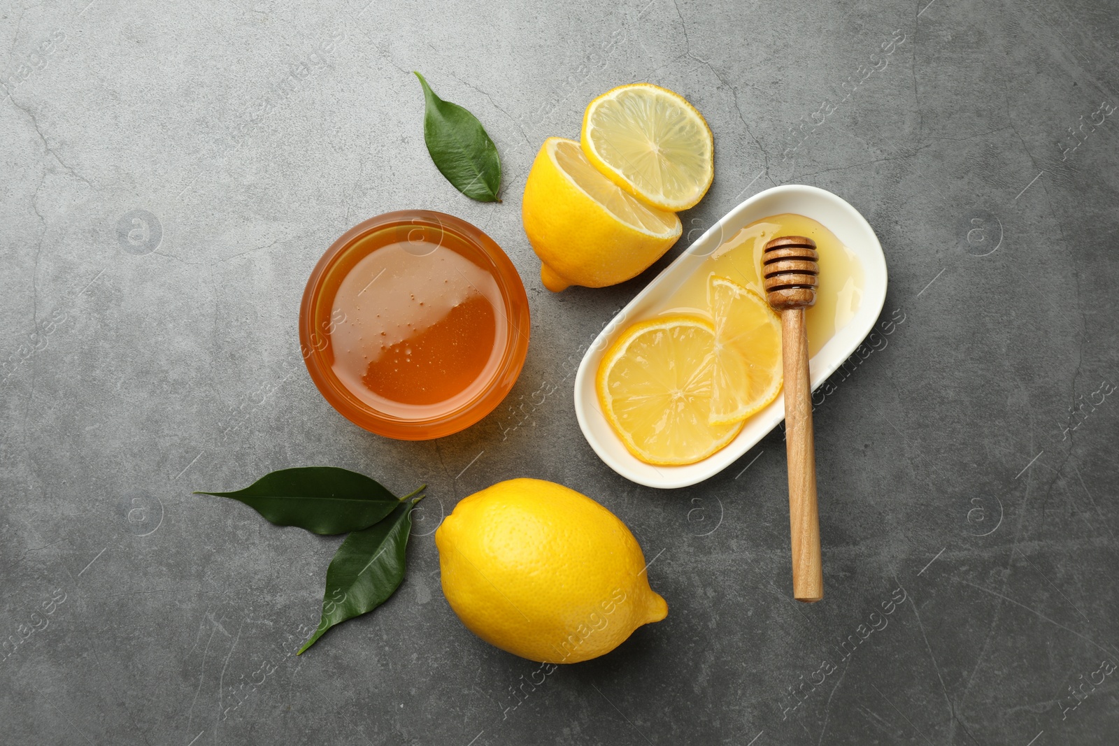 Photo of Sweet honey and fresh lemons on grey table, flat lay