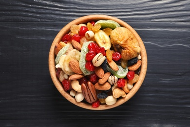 Photo of Bowl with different dried fruits and nuts on color wooden background, top view