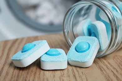 Photo of Jar with water softener tablets on wooden table near washing machine, closeup