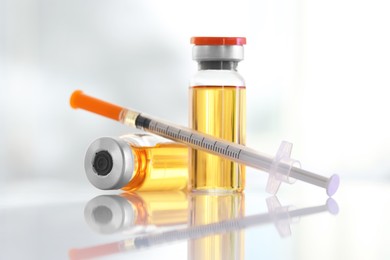 Photo of Glass vials and syringe with orange medication on white table, closeup
